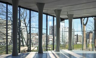 Interior view of the new La Boverie wing at Liège’s Fine Arts Museum featuring pillars and floor-to-ceiling glass windows offering a view of the trees, grass and nearby buildings outside