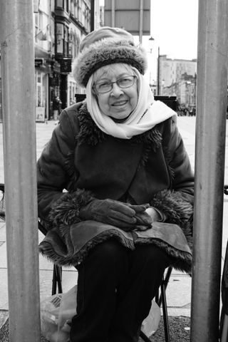 A black and white photograph of a woman sitting in between two sign posts, taken on a Fujifilm X100VI.