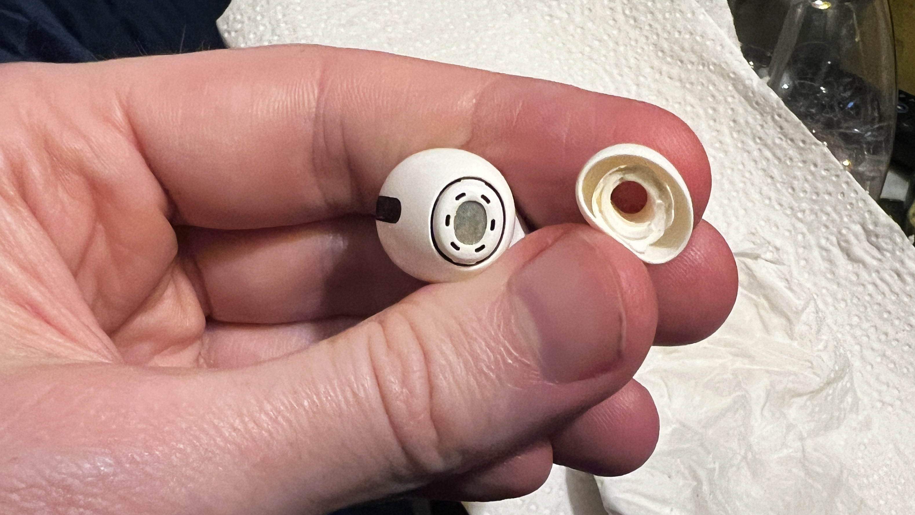 A man's hand holds an AirPods Pro 2 earbud and a tip that has torn from the earbud, leaving its connector still attached to the earbud