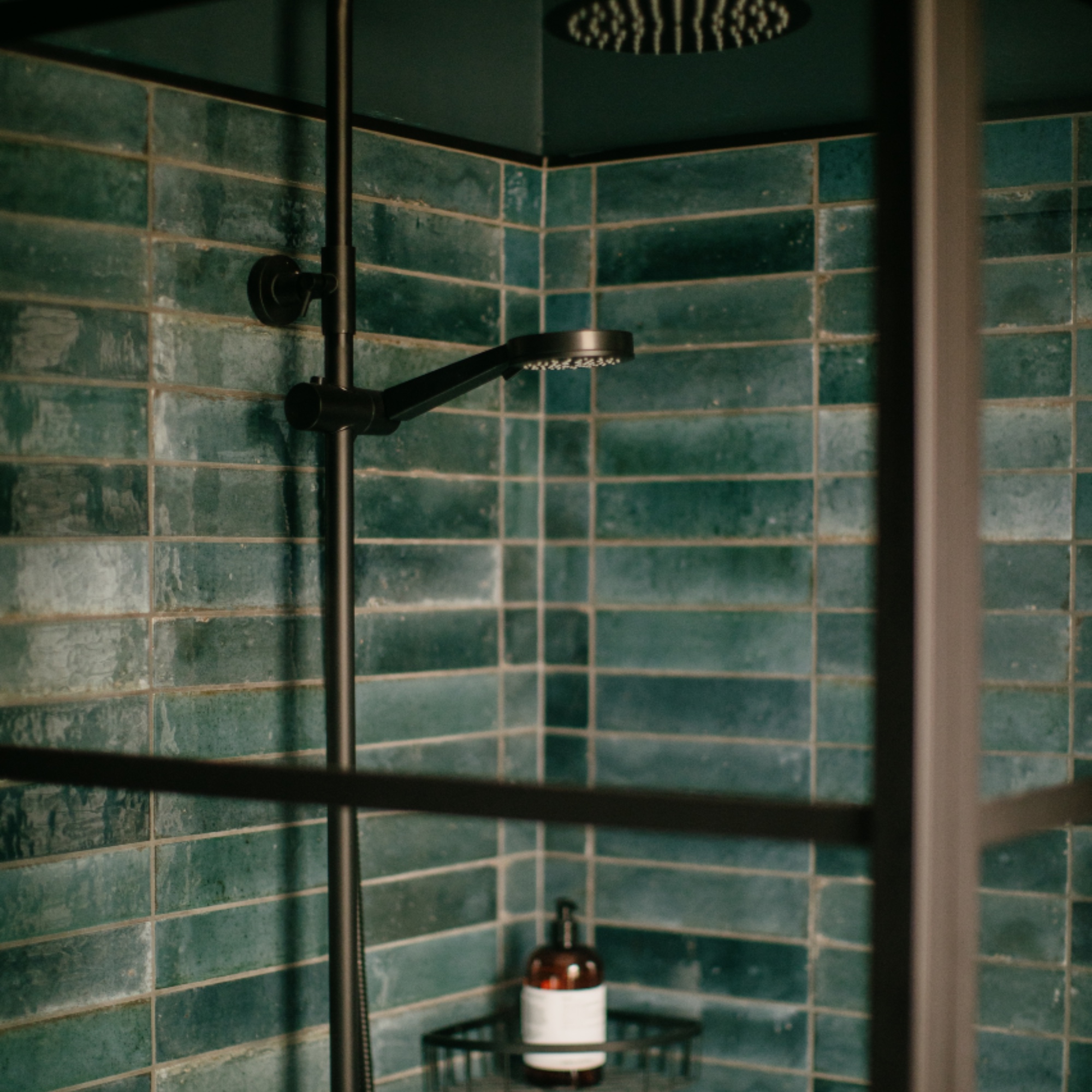 detail of shower with green metro tiles, antique brass fixtures