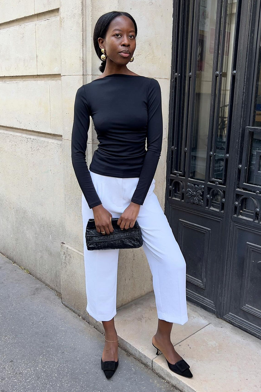 A woman wearing a black long sleeve shirt and white culotte pants with black pointed-toe shoes