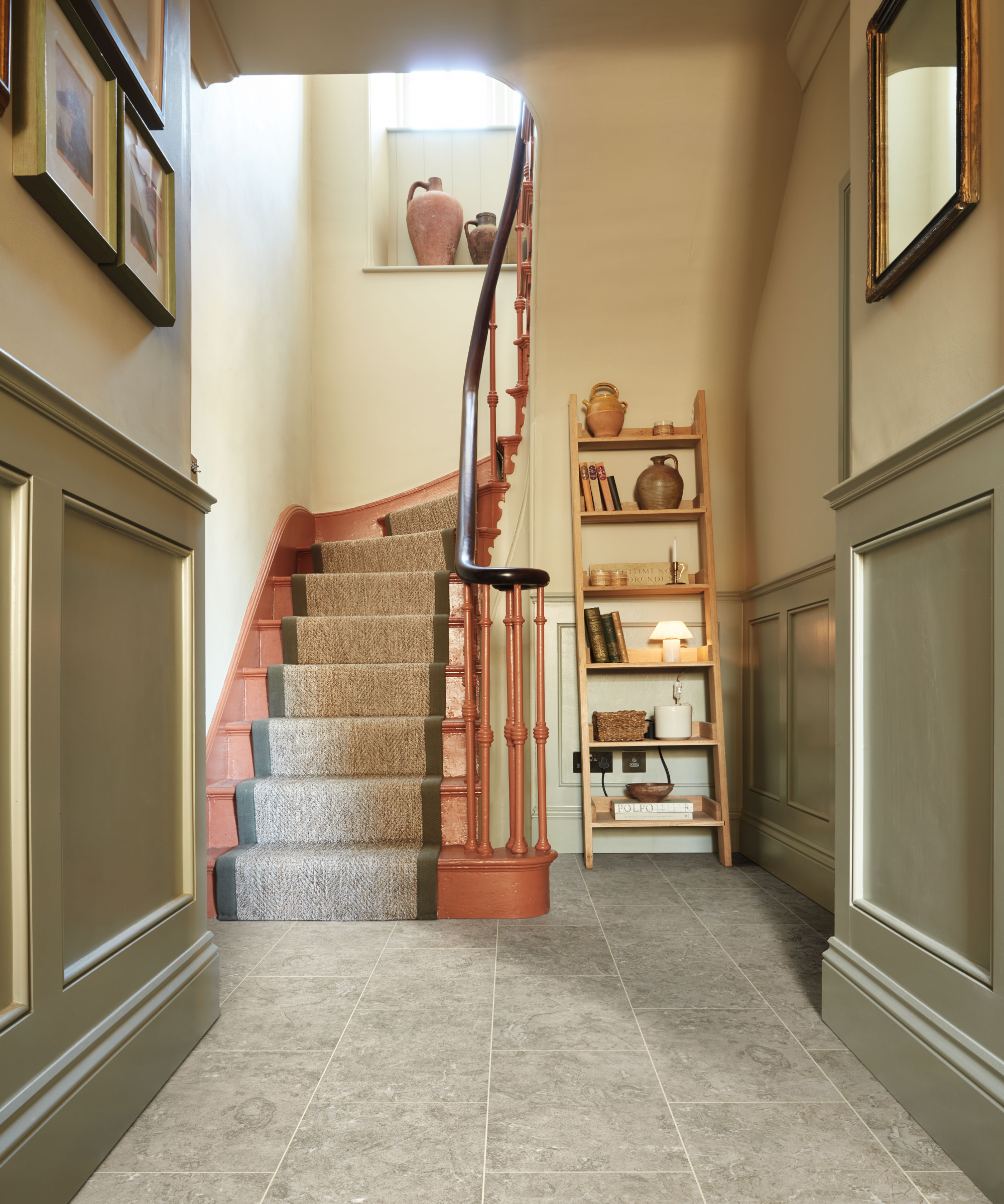 hallway with sage green panelling, light tiled effect floor and pale orange staircase with runner