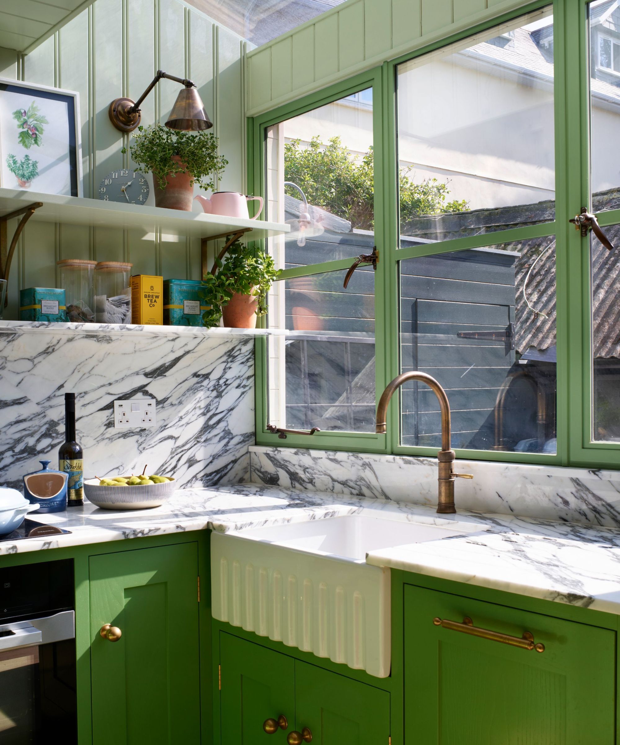 a small U-Shaped kitchen with bright green cabinets, marble countertops, and a soft green applied to the shelving and wall paneling