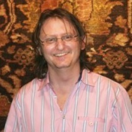 A picture of Omri Schwartz, in a pink shirt with a rug in the background