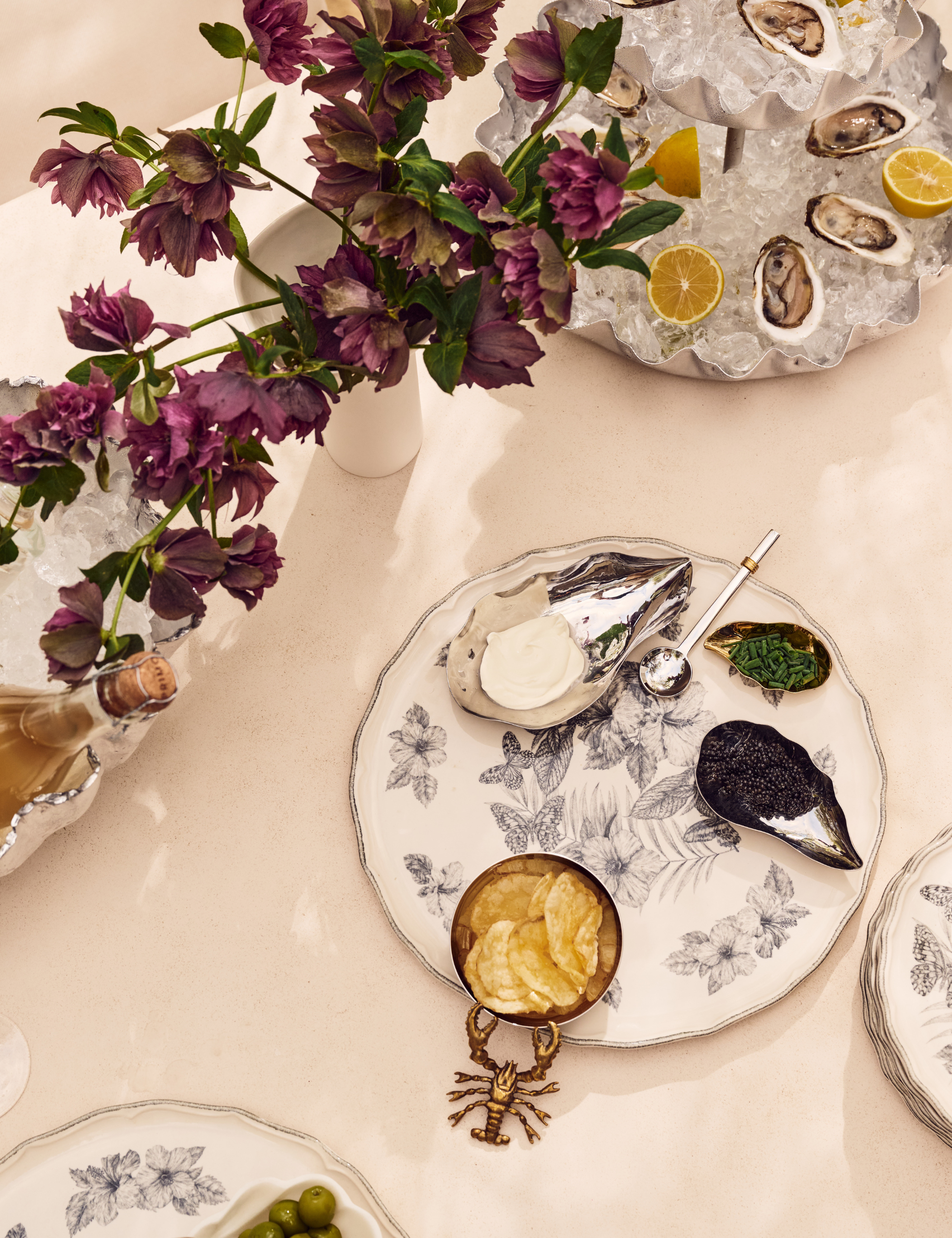 Outdoor tablescape featuring white botanically printed plates and assorted sea creature-inspired serveware.