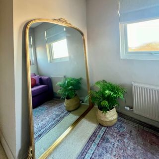 large gold leaner mirror with plant in basket