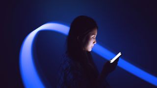 A young woman looking at a phone she is holding that is lighting up her face, stood against a dark background. Behind her, a bright ribbon of blue energy sweeps round to represent the AI sector.