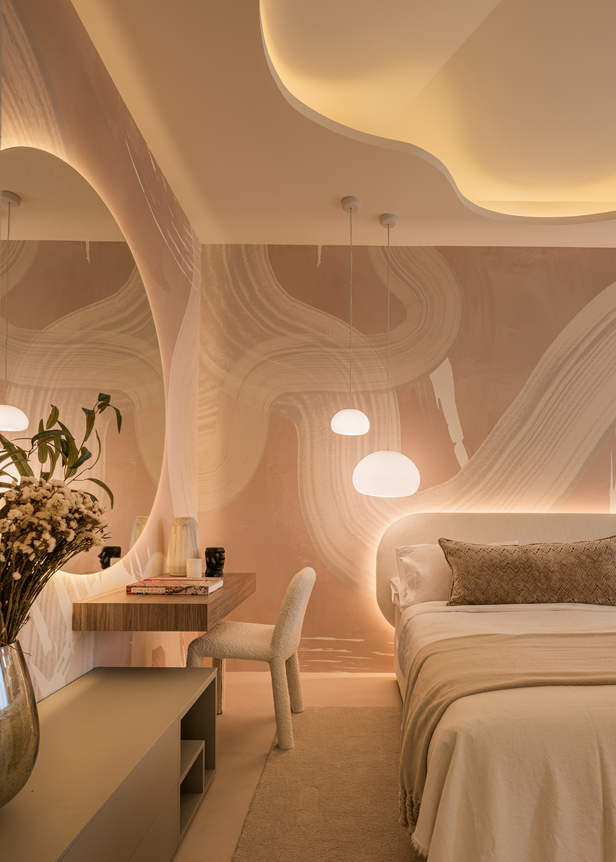 A bright bedroom with patterned walls, hanging orb lamps, a backlit headboard with a large bolster pillow and muted sheets, a floating study with a white stool, and a circular mirror