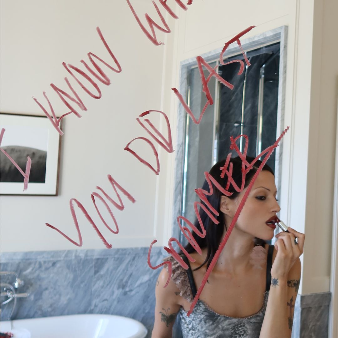 An image of Gabbriette applying her lipstick in the mirror with the words "I Know What You Did Last Summer" written in lipstick.
