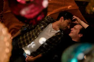 Two men (Karan Soni and Jonathan Groff) are seen lying on a bed, with colored glass ornaments around them, in 'A Nice Indian Boy.'