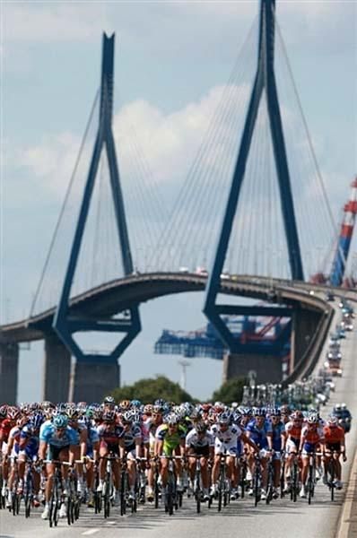 After crossing a bridge, the peloton rolls along in Hamburg, a city with a harbor on the Elbe River.