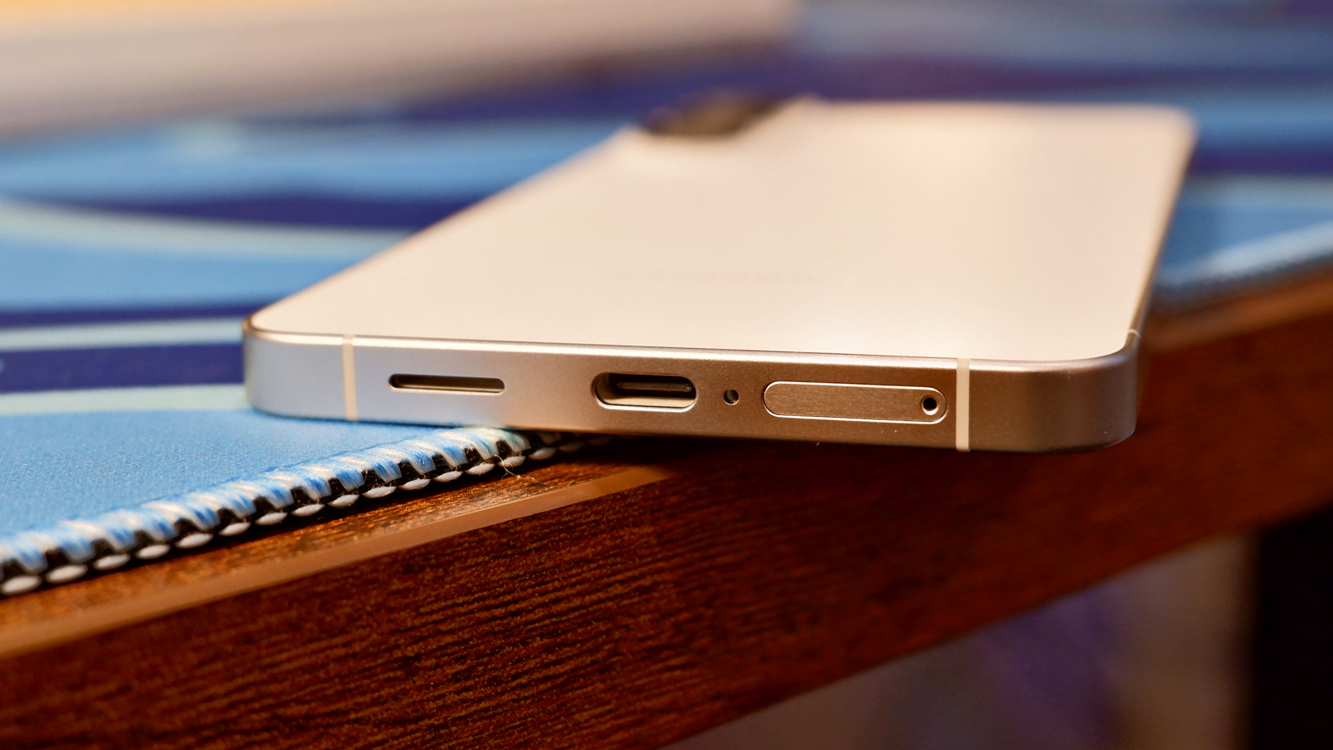 The Samsung Galaxy S26 Plus on a brown desk with blue mousepad, showcasing the USB Type-C port.