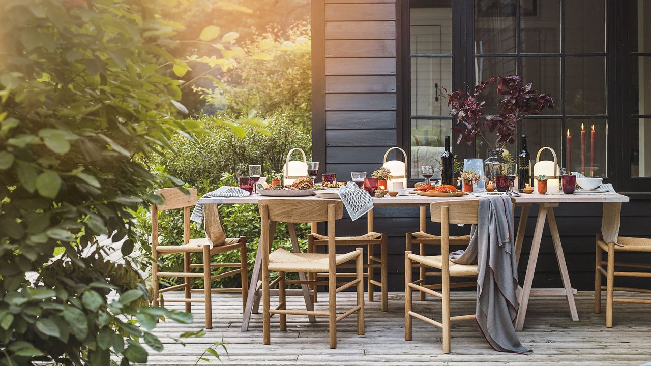 smart outdoor entertainment decked patio at sunset with dining table set for an evening meal with lamps and lighting