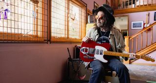 Mike Campbell pictured with his new Red Dog Fender Telecaster; the heavily customised electric guitar has a Bigsby, a Destruct button and a pickup configuration that gives you lots of options. Campbell wears shades and a wide-brimmed hat.