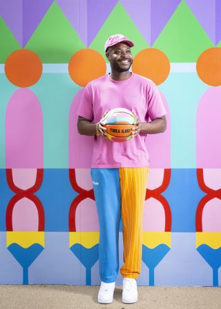 Yinka Ilori holding a colourful basketball at the basketball court he designed for London's Canary Wharf Estate, May 2021
