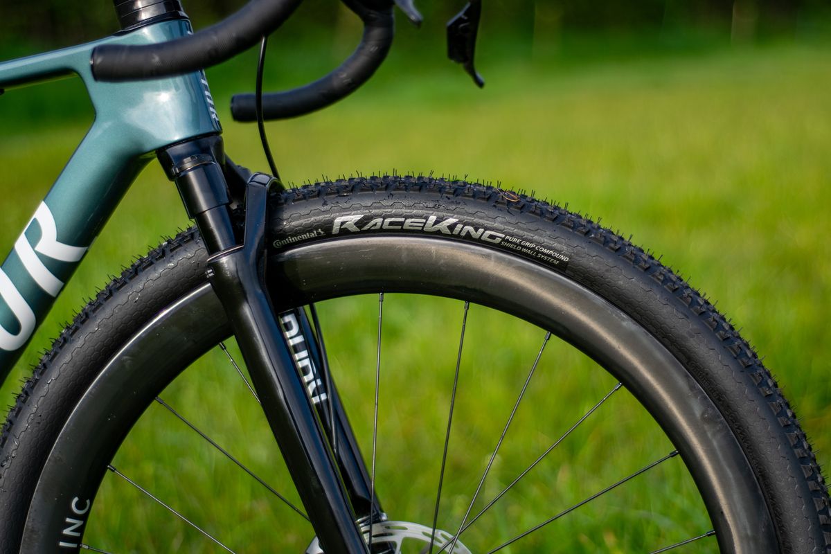 A blue Factor Sarana gravel bike in a grassy field with a hedge in the background