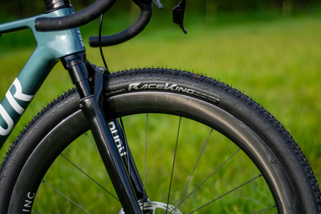 A blue Factor Sarana gravel bike in a grassy field with a hedge in the background