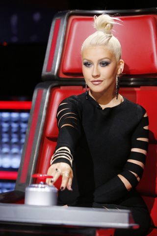 Christina Aguilera hovers her hand over a large red button on a TV show.