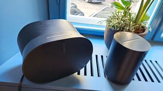 En svart Sonos Era 300 och Sonos Era 100 står på ett fönsterbräde.