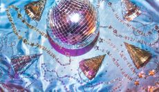 New Year's Eve background with party favors that include a disco ball, party hats, glittering star confetti, and novelty beaded necklaces. 