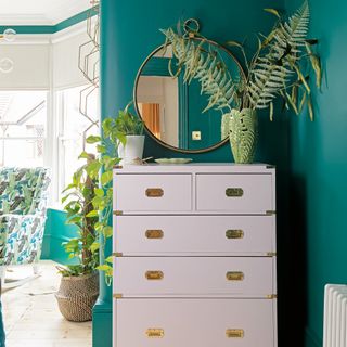Pink chest of drawers in green room with mirror and plants