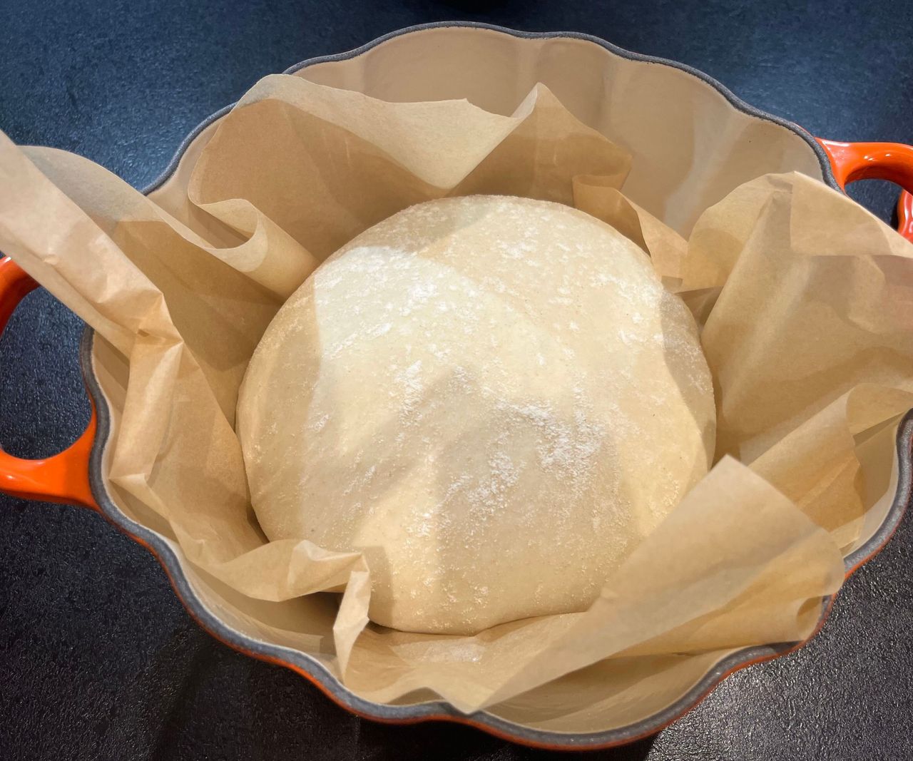 An orange Le Creuset Pumpkin cocotte on a black kitchen counter, with bread dough insde before baking.