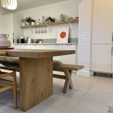 kitchen with neutral floor tiles, white cabinetry and wood table with bench. 