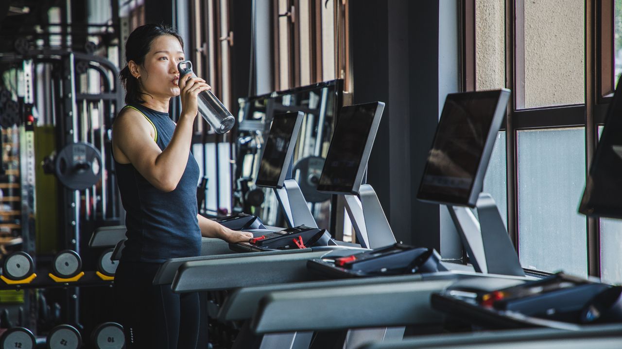 Woman drinking from a water bottle after a treadmill session