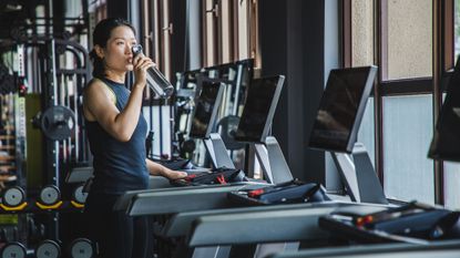 Woman drinking from a water bottle after a treadmill session