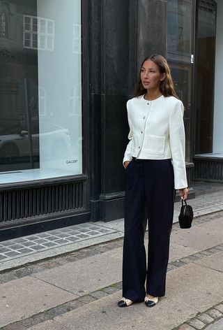 a photo showing what shoes to wear with wide-leg pants with a woman on the sidewalk wearing a white tweed jacket with black wide leg pants and two-tone tan and black ballet flats