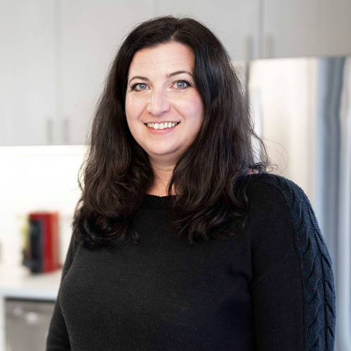 Brooke Stafford smiling, in black sweater, pictured in front of out-of-focus kitchen.