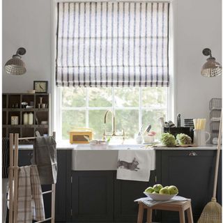 built in worktop and storage cupboards with washbasin, wooden stool and clothes rack, striped Roman blind
