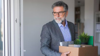 A laid-off mature office worker carries his belongings in a box as he leaves.