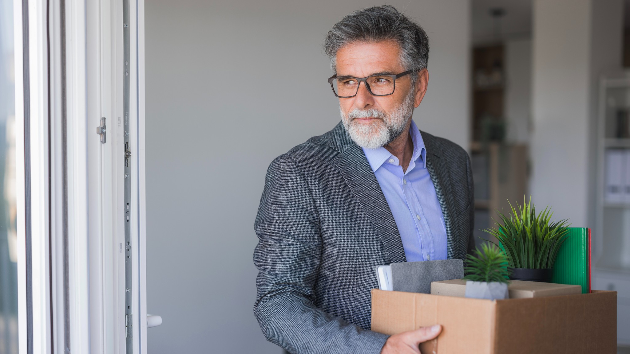 A laid-off mature office worker carries his belongings in a box as he leaves.