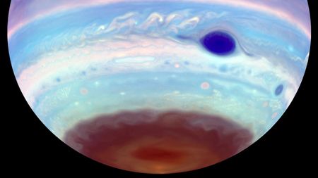 The southern hemisphere of Jupiter hangs from above in black space, striped in false color blues, violets, and dark reds