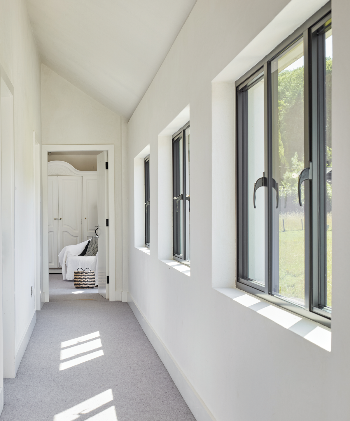 Hallway with windows to the right and bedroom behind a door at the end