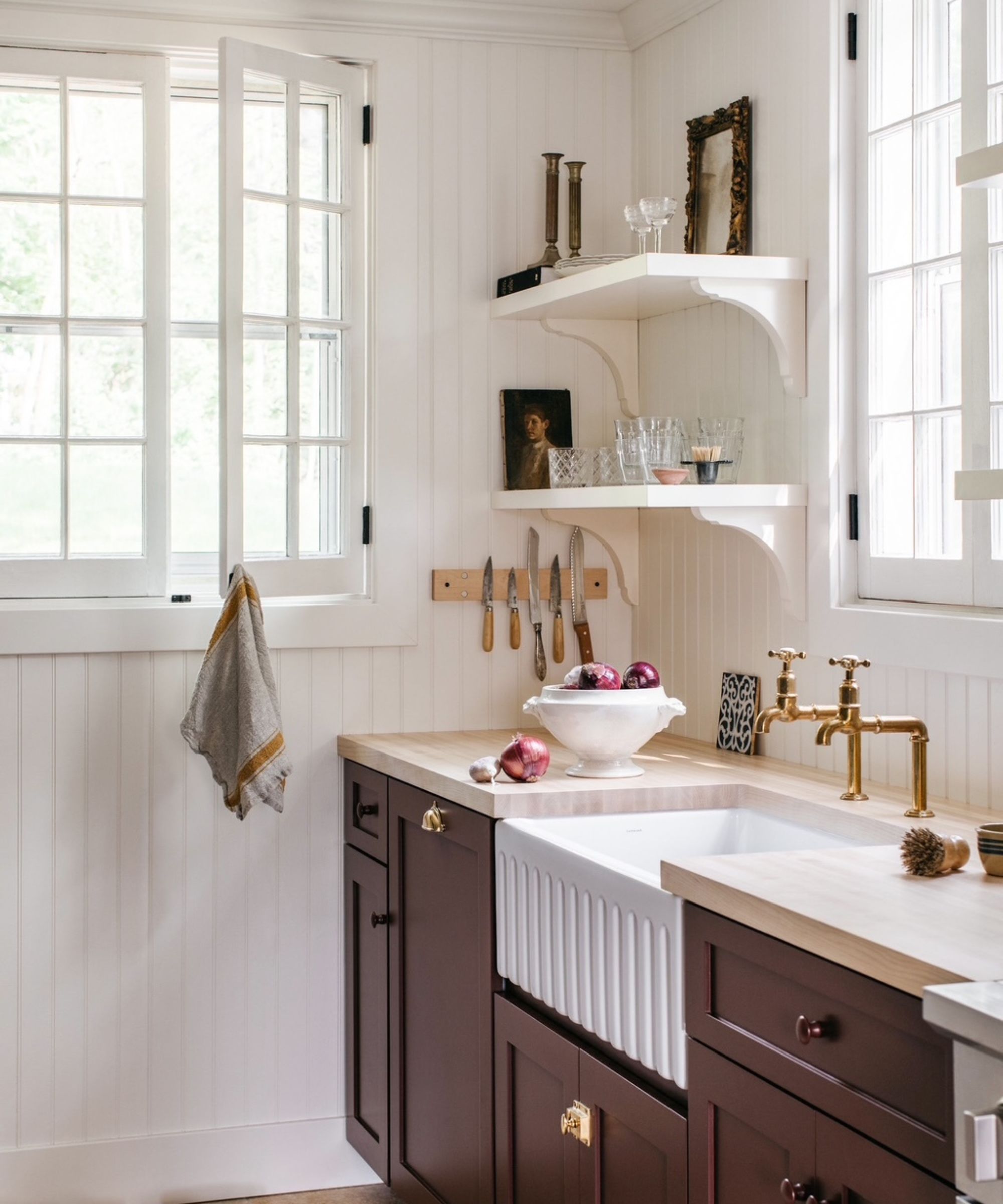 A cottage kitchen with white paneled walls, burgundy cabinets, white open shelves and wooden countertops