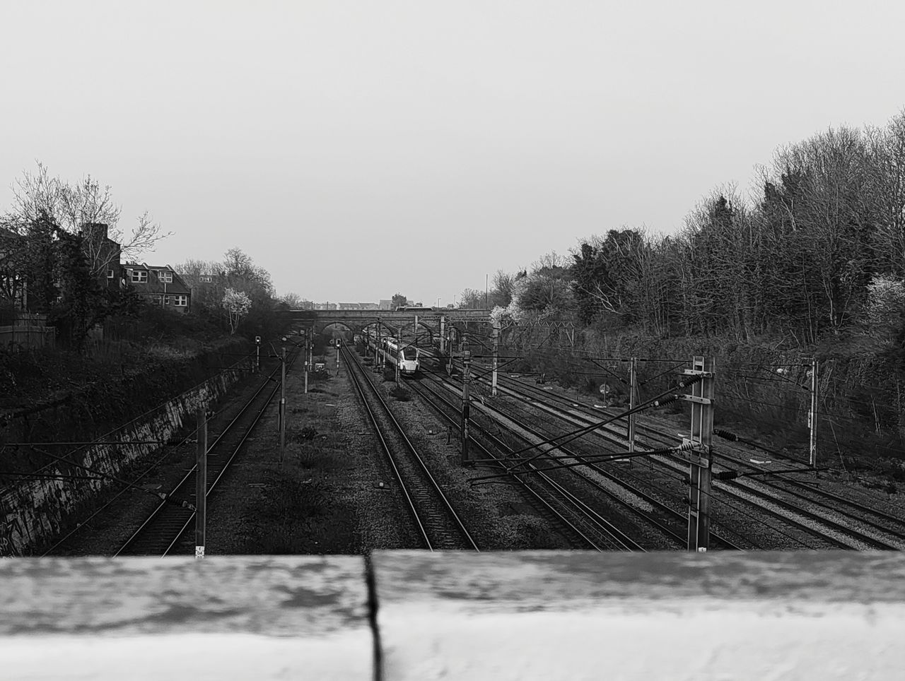 Black-and-white photo of railway tracks stretching toward a distant bridge with a train approaching, photographed with the Nothing Phone (4a).