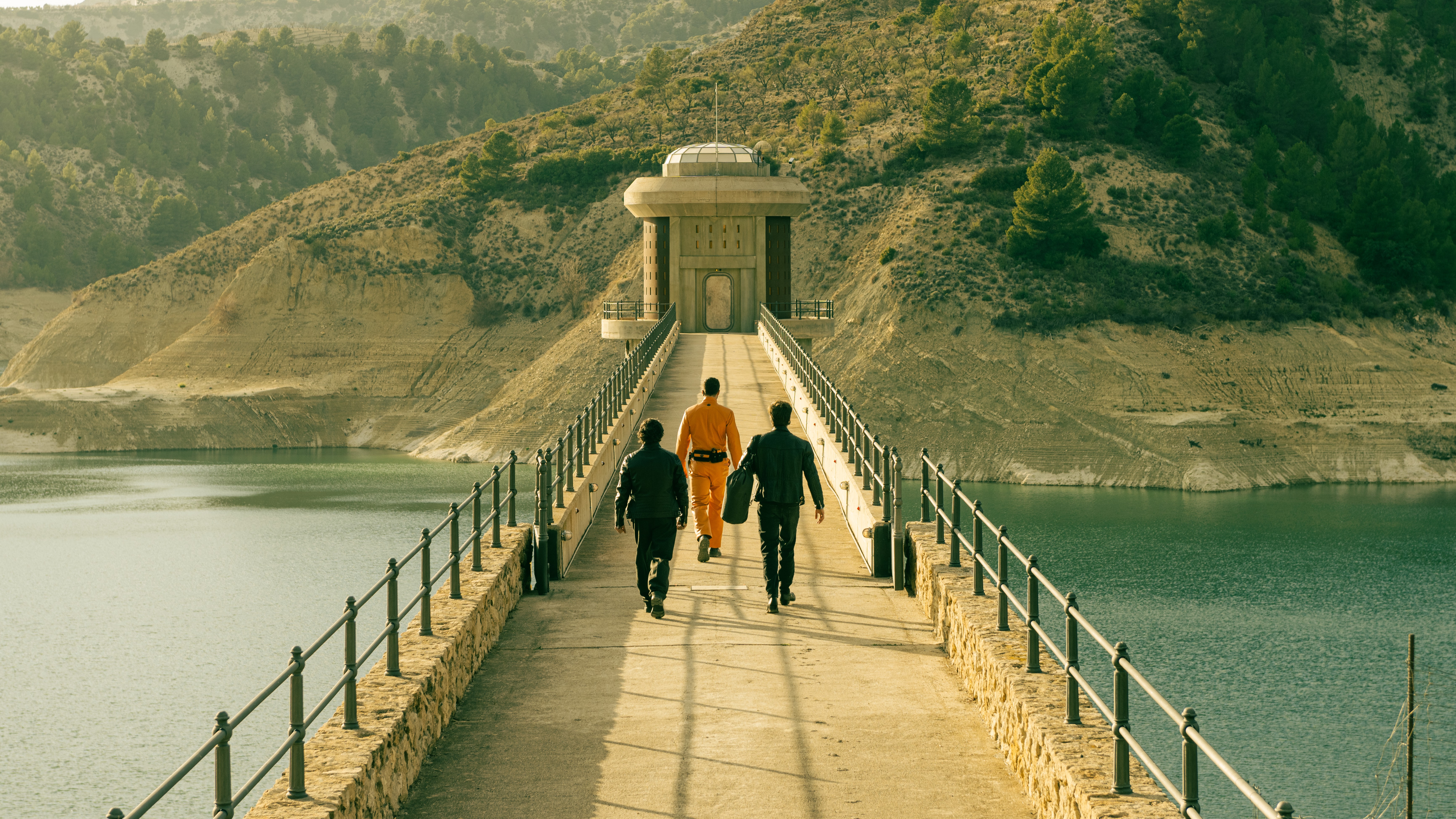 A scene from Netflix's "Billionaires' Bunker" featuring three figures (facing away from the camera) walking across a bridge