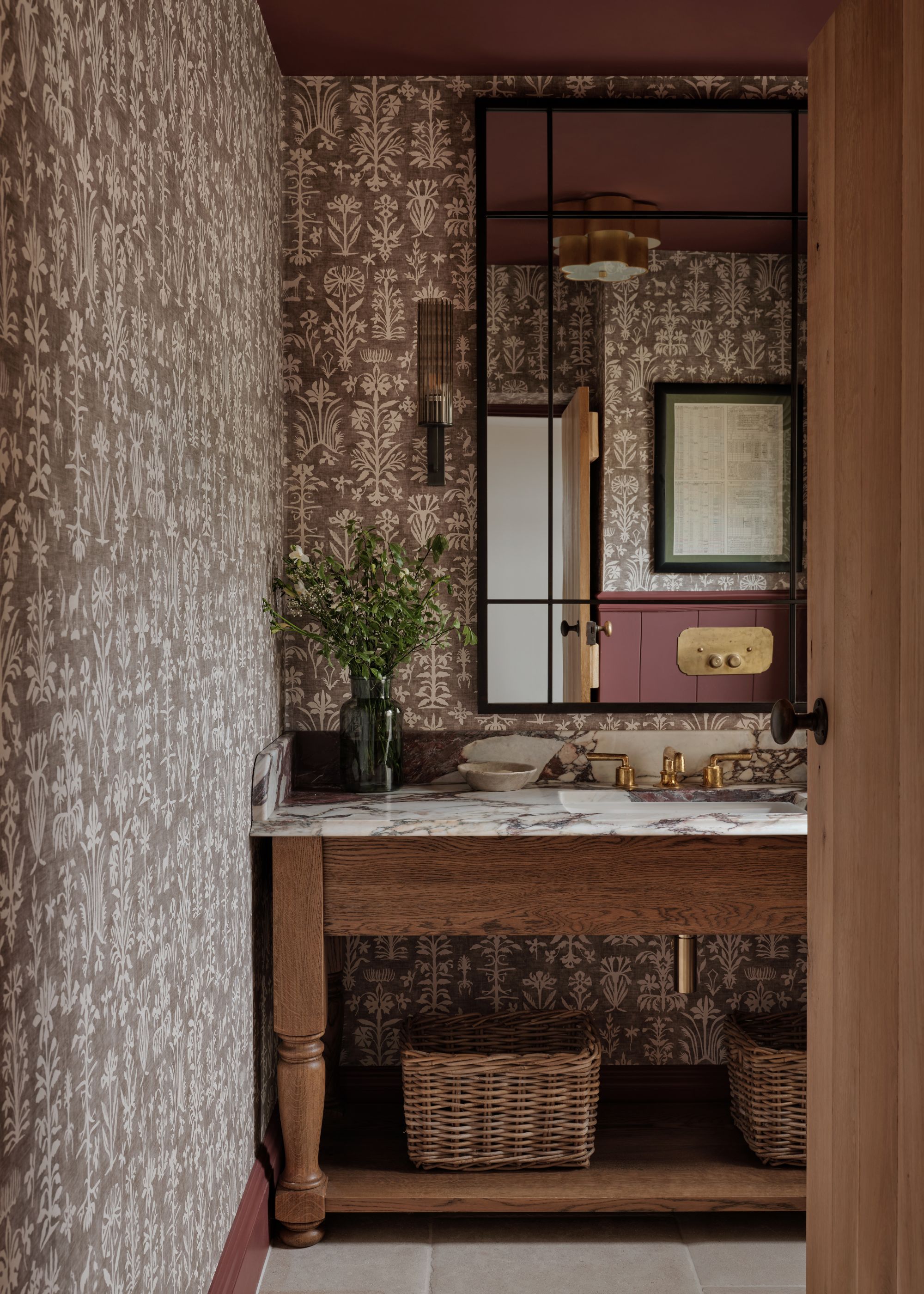 A cloakroom with maroon-patterned wallpaper and a maroon-painted ceiling, a wooden vanity with a marble countertop, and a large mirror.