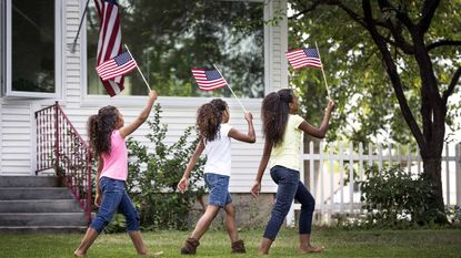 three young girls walking in front of white house holding american flags