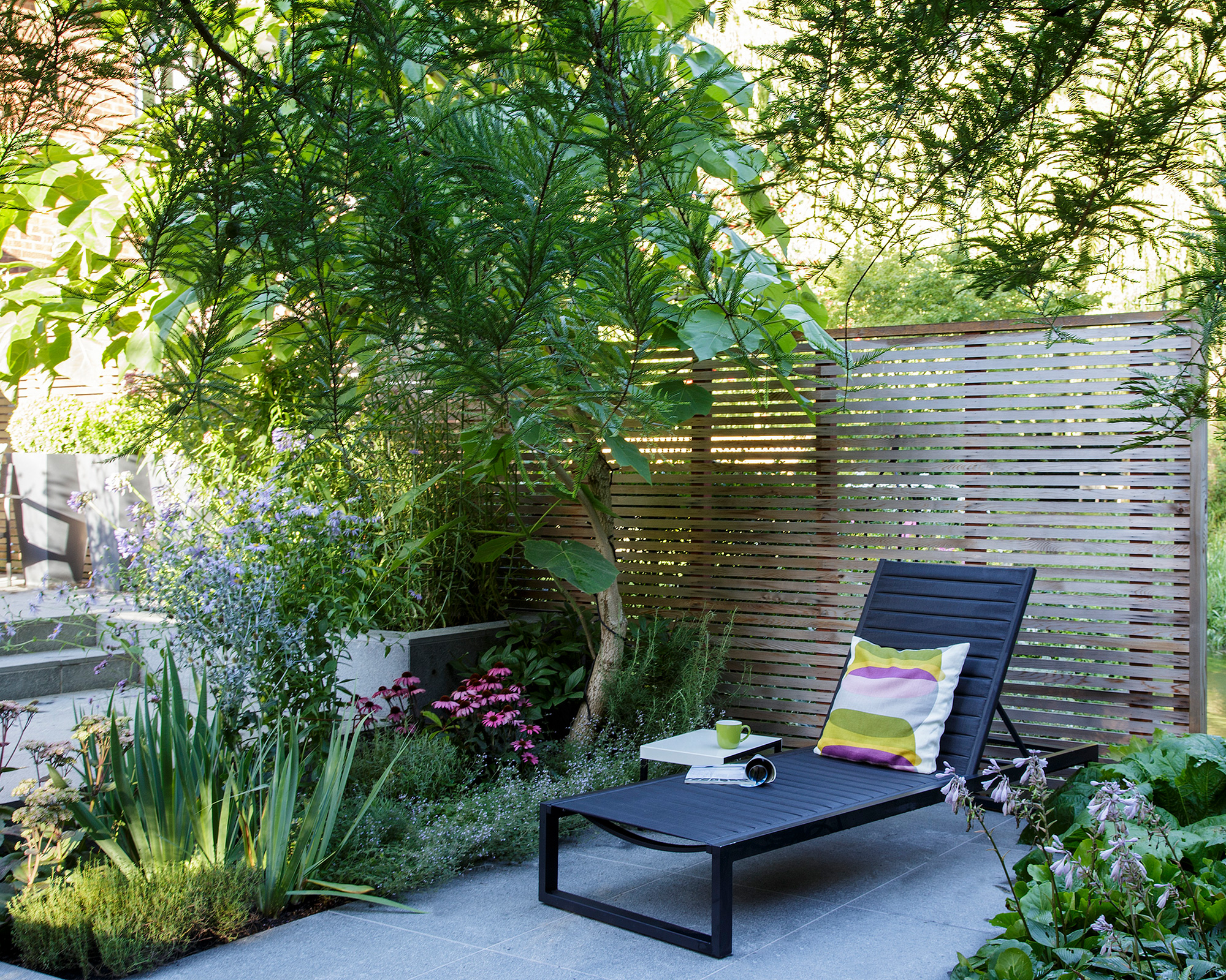 Patio planting ideas in a shaded garden with sun lounger and screened fence.