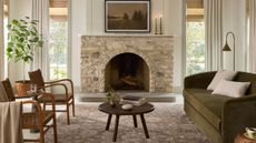 Joanna Gaines x Loloi vintage-inspired patterned rug photographed in a sunlit living room with a green couch, stone fireplace, and tall windows