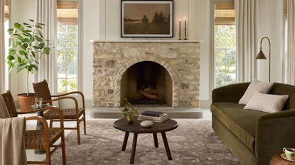 Joanna Gaines x Loloi vintage-inspired patterned rug photographed in a sunlit living room with a green couch, stone fireplace, and tall windows