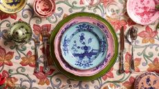 A heavily patterned, colourful, embroidered tablecloth with a colourful table setting from Mytheresa Life.