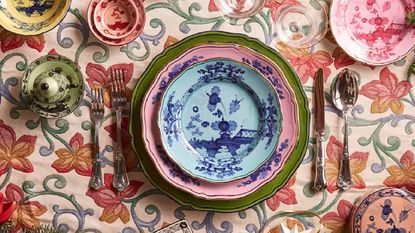 A heavily patterned, colourful, embroidered tablecloth with a colourful table setting from Mytheresa Life.
