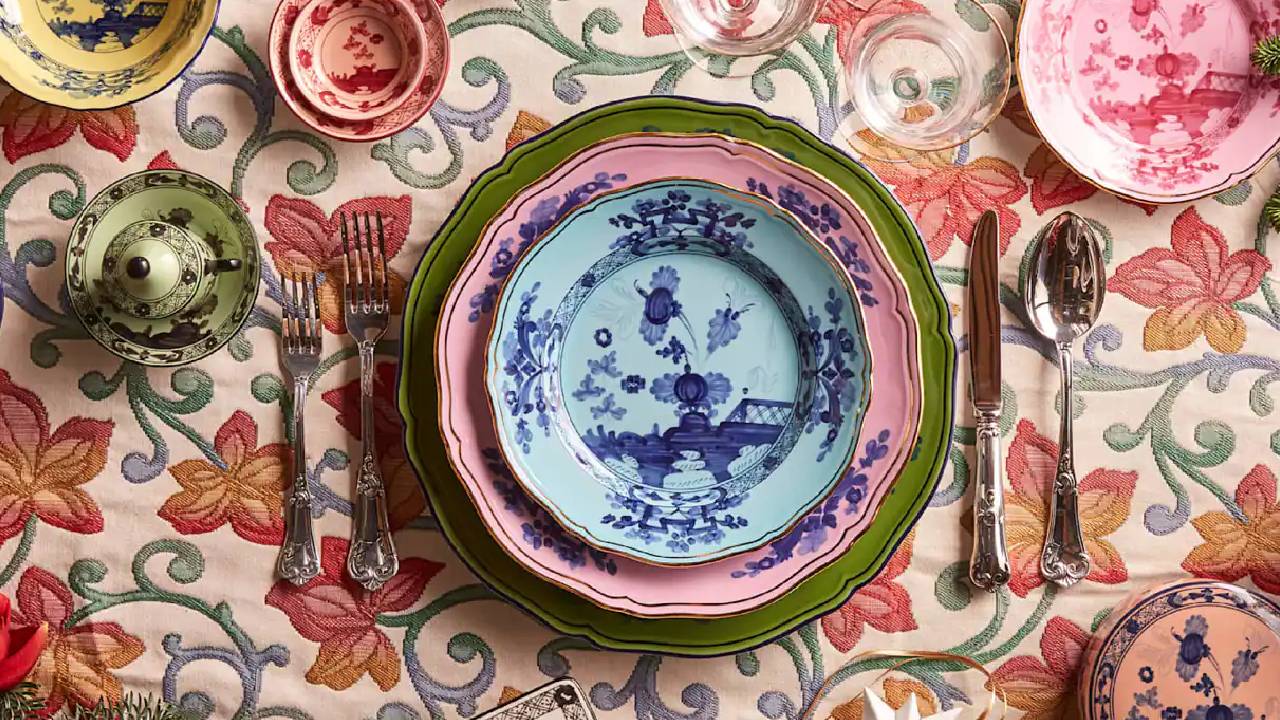 A heavily patterned, colourful, embroidered tablecloth with a colourful table setting from Mytheresa Life.