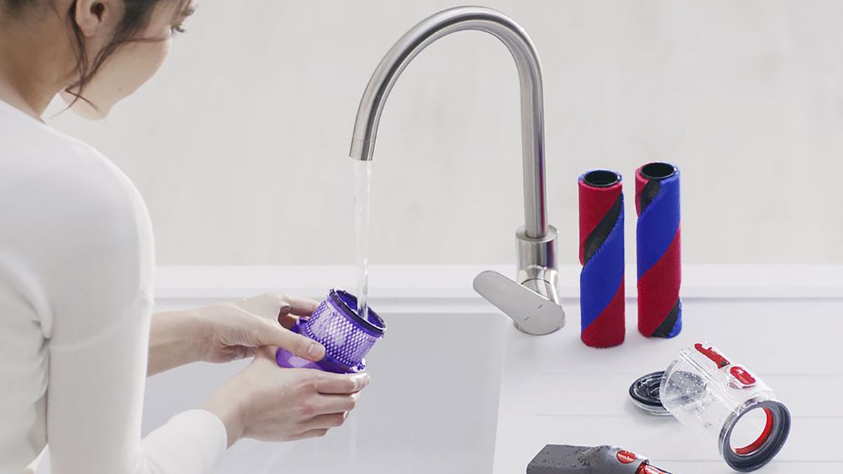 Woman cleaning the parts of a Dyson vacuum in a sink.