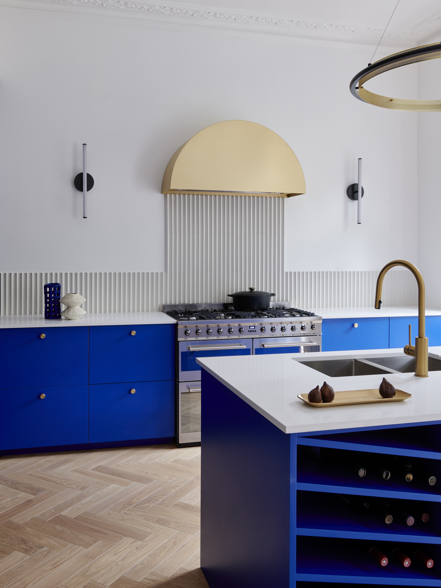 Image of a modern kitchen with white walls and electric blue cabinetry. There is a white ribbed backsplash and a golden hutch above the stove.