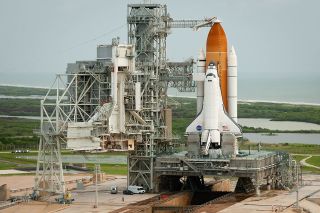 space shuttle next to a launch tower with swamp in behind